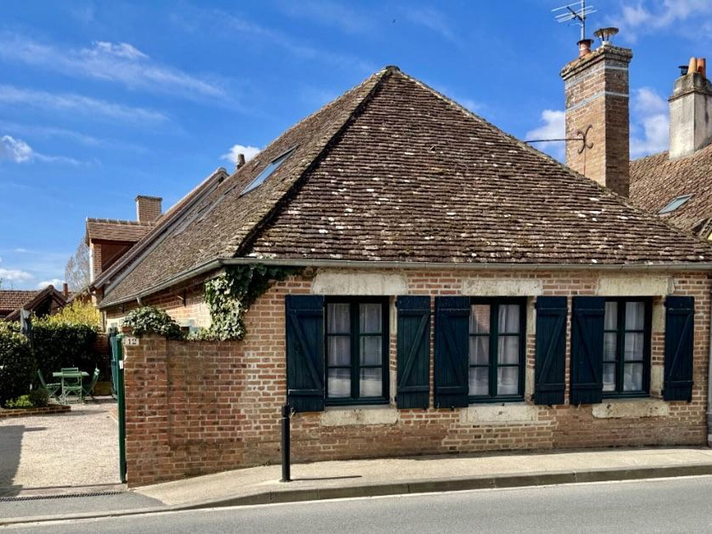 Un edificio de ladrillo con techo a dos aguas, chimenea y una ventana con contraventanas.
