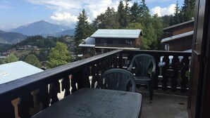 Ein Balkon mit Tisch und Stühlen, mit Blick auf eine gebirgige Landschaft mit Häusern und Bäumen.