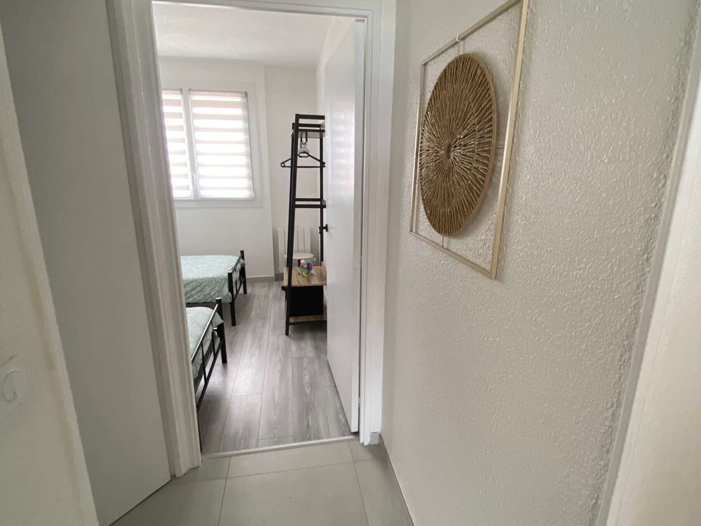 Um corredor estreito que leva a um quarto, com uma cama, uma escada de madeira e uma decoração na parede emoldurada.