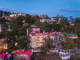 Un hotel de varios pisos con balcones, rodeado de árboles y otros edificios.