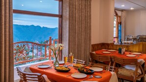 A dining area with a mountain view, wooden furniture, and a table set for two. - PACK Shimla (Shimla)