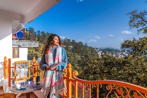 A balcony with a view of a mountainous landscape, a table with a cup and a book, and a person holding a book.