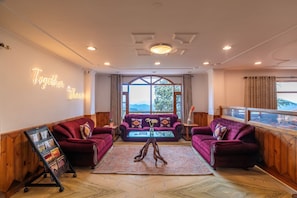 A room with two red sofas, a wooden floor, a large window with a view, and a neon sign on the wall.