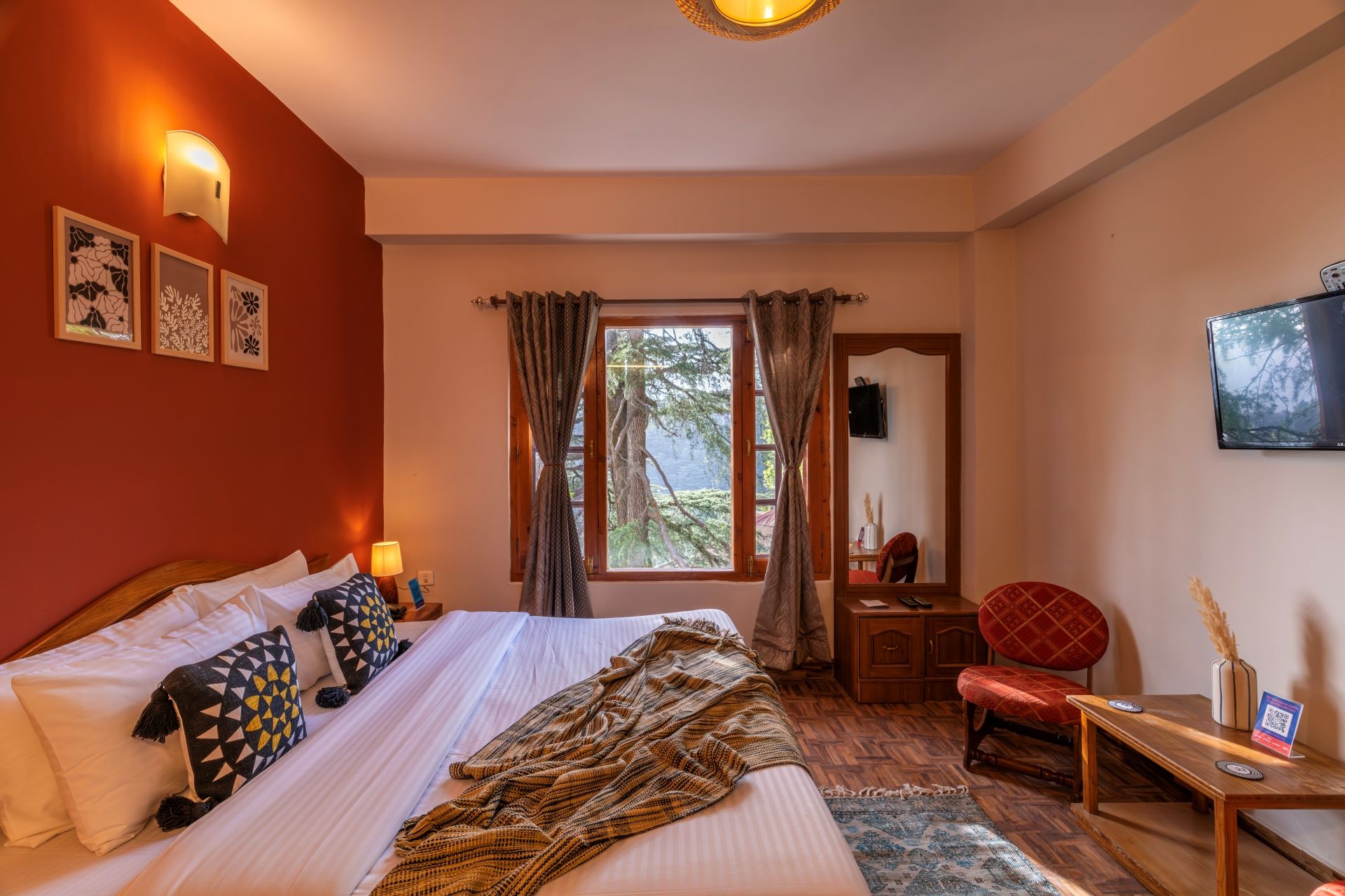 A hotel room with a bed, a desk, a chair, a window with curtains, and wall-mounted artwork.