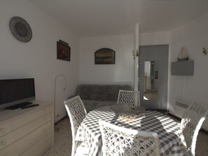 Ein Essbereich mit einem karierten Tisch, weißen Stühlen, einem Fernseher auf einem Schrank und einem Gemälde an der Wand.