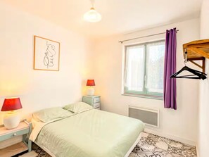 A bedroom with a bed, bedside lamps, a window with curtains, a radiator, and a wall-mounted coat rack. - Central house, pets welcome - 4 guests (La Roche-Posay)
