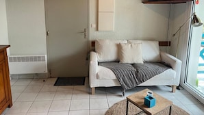 A living room with a white sofa, a small coffee table, a television mounted on the wall, and a door. - Mezzanine apartment near ocean - 4 guests (Capbreton)