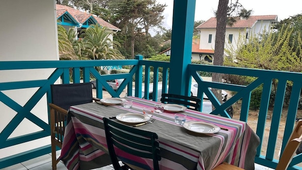 A covered outdoor dining area with a table set for four, chairs, and a view of surrounding buildings. - Mezzanine apartment near ocean - 4 guests (Capbreton)