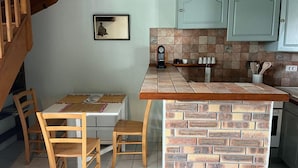 A kitchen with a wooden island, a dining table with chairs, light-colored cabinets, and a clock on the wall. - Mezzanine apartment near ocean - 4 guests (Capbreton)