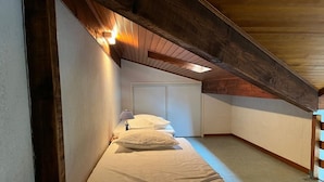A bedroom with a sloped ceiling, a bed with white bedding, a nightstand, and a wall-mounted lamp. - Mezzanine apartment near ocean - 4 guests (Capbreton)