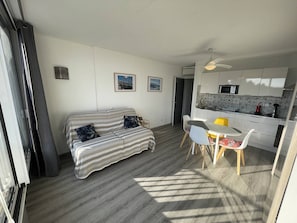 Ein modernes Wohnzimmer mit einer Couch, einem Esstisch mit Stühlen, einer Küchenzeile inklusive Schränken und einer Mikrowelle sowie einem Deckenventilator.