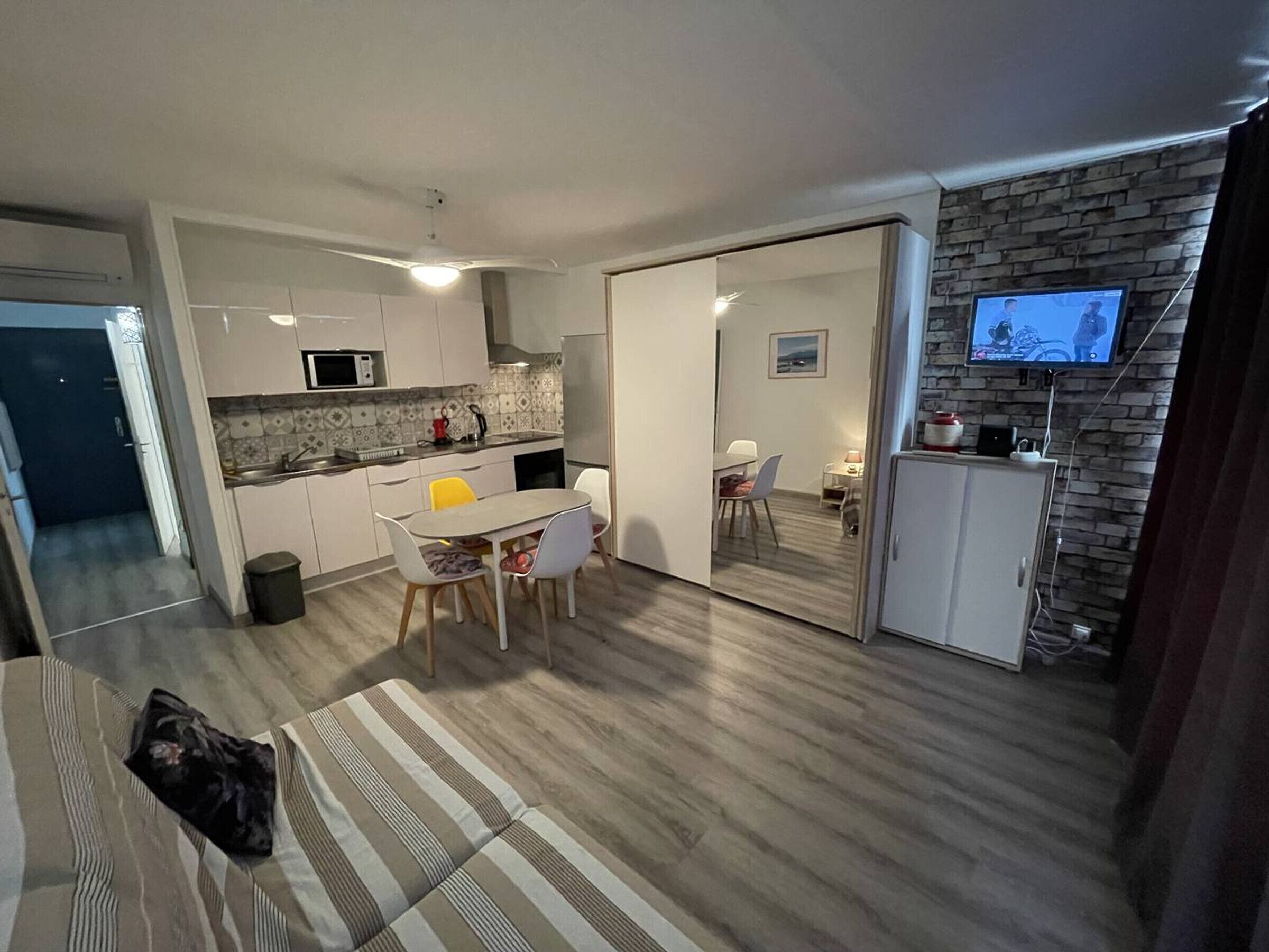 Un espace de vie compact comprenant une cuisine, un coin repas et un téléviseur fixé à un mur en briques.