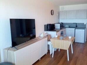 A compact living space with a flat-screen TV, a kitchenette, a dining area with a table and chairs, and a small kitchen with appliances. - Studio cabin, AC, sea view - 5 guests (Canet-Plage)