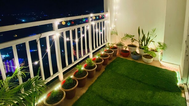 Ein Balkon mit Geländer, Pflanzkübeln, Kunstgrasturf und Lichterkette.