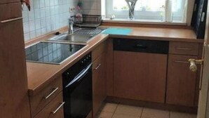 Uma cozinha compacta com lava-louças, forno e janela com vista para árvores.