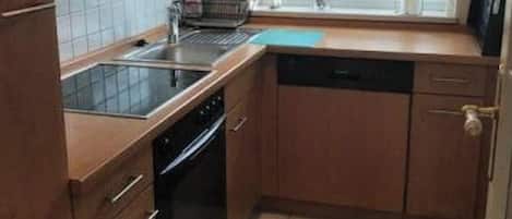 Cocina compacta con lavavajillas, horno y ventana con vistas a árboles.