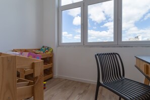 A room with a wooden playpen, a black chair, and a window with a city view. - 4BR Duplex w Rooftop Views Workspaces (Lisbon)