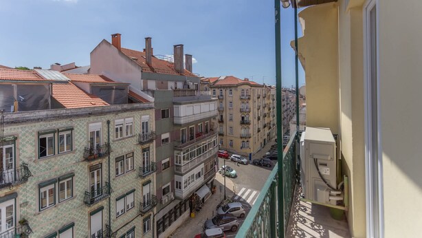 A balcony with a view of multi-story buildings, a street with parked cars, and a clear sky. - 4BR Duplex w Rooftop Views Workspaces (Lisbon)