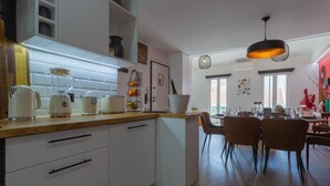 A modern kitchen with white cabinets, a wooden countertop, and a dining area with two chairs and a table. - 4BR Duplex w Rooftop Views Workspaces (Lisbon)