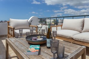 A rooftop terrace with a wooden table, two cushioned chairs, a bottle, and a magazine. - 4BR Duplex w Rooftop Views Workspaces (Lisbon)