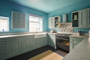 Una cocina con paredes verde azulado, una ventana, armarios, una estufa y un salpicadero con diseño.