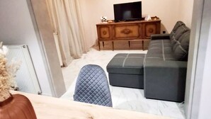 Una sala moderna con un sofá, un reposapiés y un televisor sobre un mueble de madera.