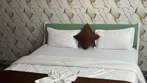 Una cama bien hecha con ropa blanca, una almohada marrón y una toalla blanca.