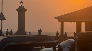 Vista al atardecer con un faro, un muelle y gente junto al agua.