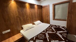 A bedroom with a wooden headboard, a bed with white bedding, a patterned throw blanket, and a window with a wooden frame. - Hotel Star (Shivpuri)