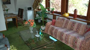 A living room with a sofa, a glass coffee table, a potted plant, a small table with a lamp, and a window with curtains. - Vacation apartment panoramablick ( 85 m2 - 5 persons.) (Lennestadt)