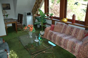 Ein Wohnzimmer mit einer Couch, einem Glastisch, einer Zimmerpflanze und Blick durch ein Fenster.