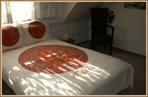 Ein Schlafzimmer mit einem Bett, Kissen, einem Sessel, einem Nachttisch und einer Lampe.