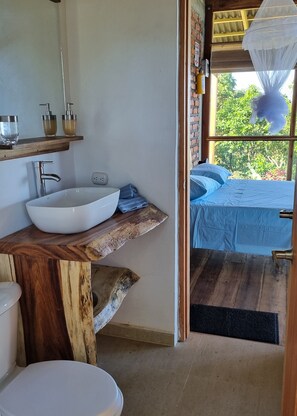 Baño con tocador de madera, lavamanos blanco y retrete.
