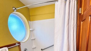 A bathroom with a bathtub, a towel rack, a circular mirror, and a shower curtain.