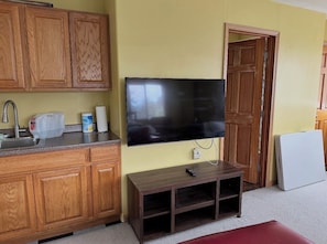 A kitchen with wooden cabinets, a built-in TV, a small wooden table, and a white refrigerator.