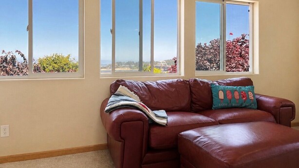 A living room with a brown leather sofa, a window with a view of trees, and a cushion with a quote.