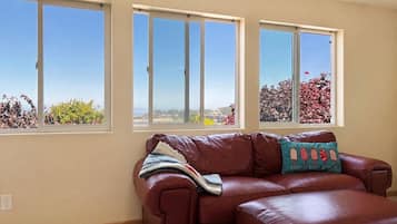 A living room with a brown leather sofa, a window with a view of trees, and a cushion with a quote.