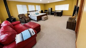 A room with a bed, a red sofa, a small table, a chair, a TV, and a fireplace.