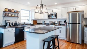 A modern kitchen with white cabinets, stainless steel appliances, a central island, and a hanging light fixture. - Spacious Summer Oaisis 4-bedroom house with AC in Kerhonkson (Kerhonkson)