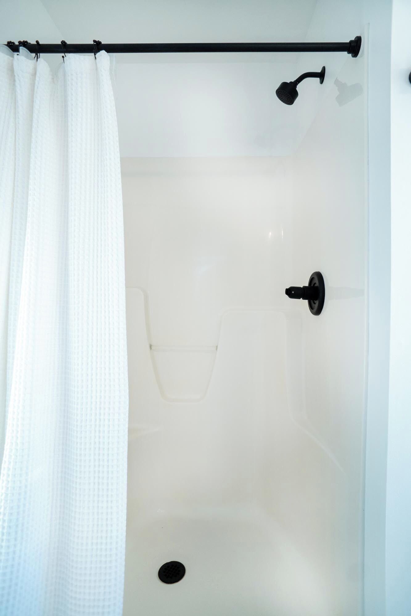 Un espace de douche blanc avec une pomme de douche noire et une poignée noire.