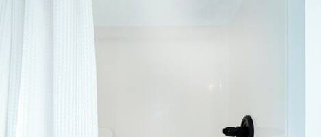 Un espace de douche blanc avec une pomme de douche noire et une poignée noire.