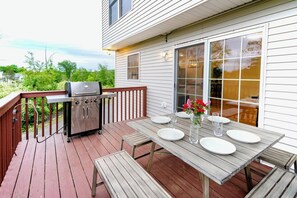 Eine Terrasse mit Grill, einem Tisch für vier Personen und Blick auf das Haus.