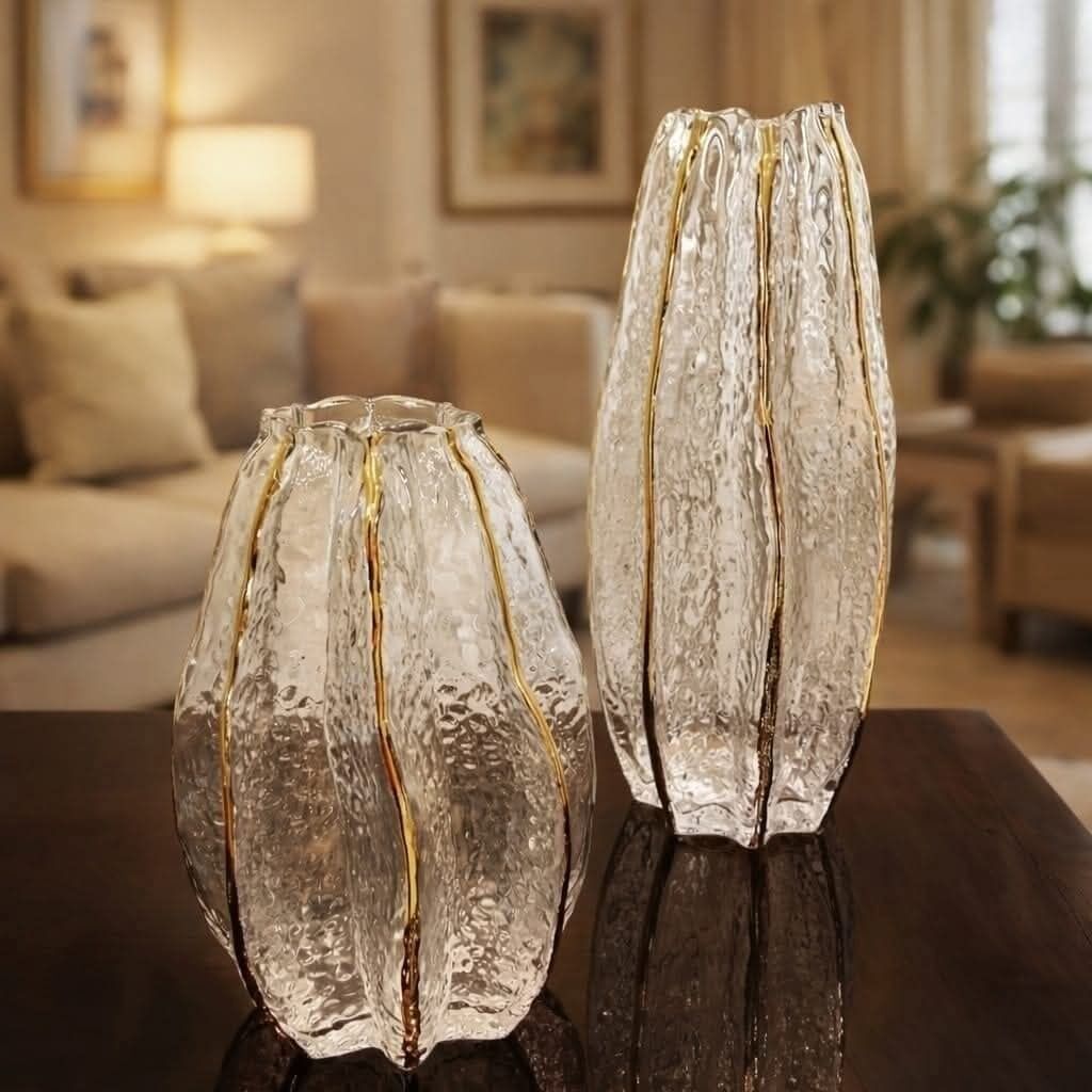 Two glass vases on a reflective surface in a room with a sofa and a painting in the background.
