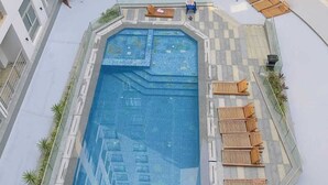 Una piscina en la azotea con suelo a cuadros, rodeada de sillones de descanso y una pequeña zona de estar.