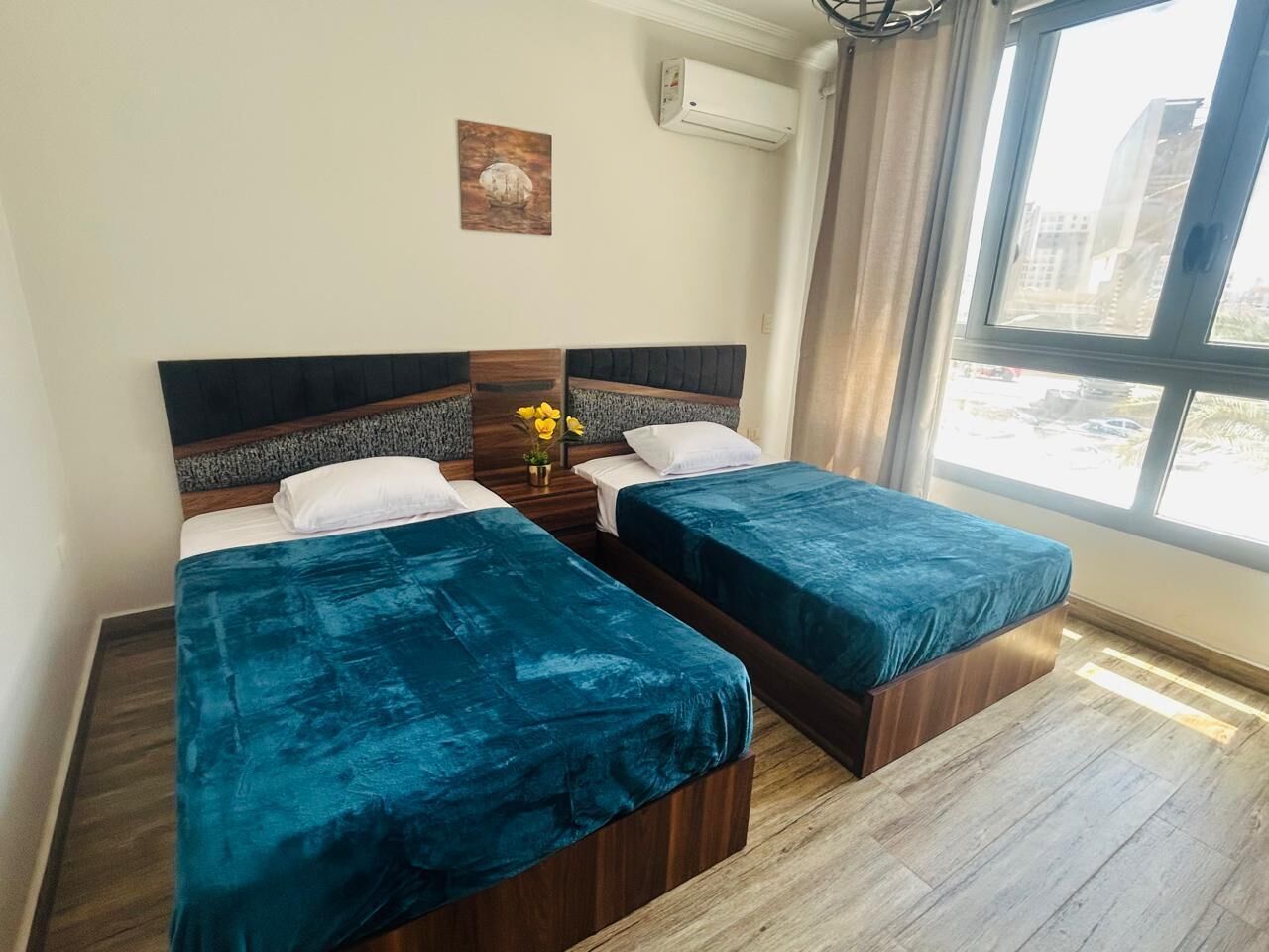 A room with two beds, a window, and a wall-mounted air conditioner.