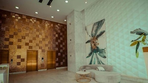 Un hall con pared de diseño, un cuadro abstracto de gran tamaño, un sofá y una mesita redonda.