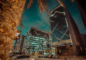 A modern building with a glass facade and geometric patterns, surrounded by palm trees and streetlights. - Premiere Cairo Apartments & Studios (Cairo)