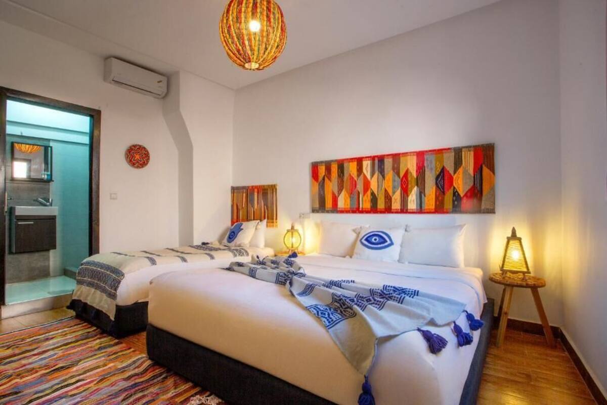 A hotel room with a large bed, a small table, a wall-mounted artwork, and a door leading to a bathroom.