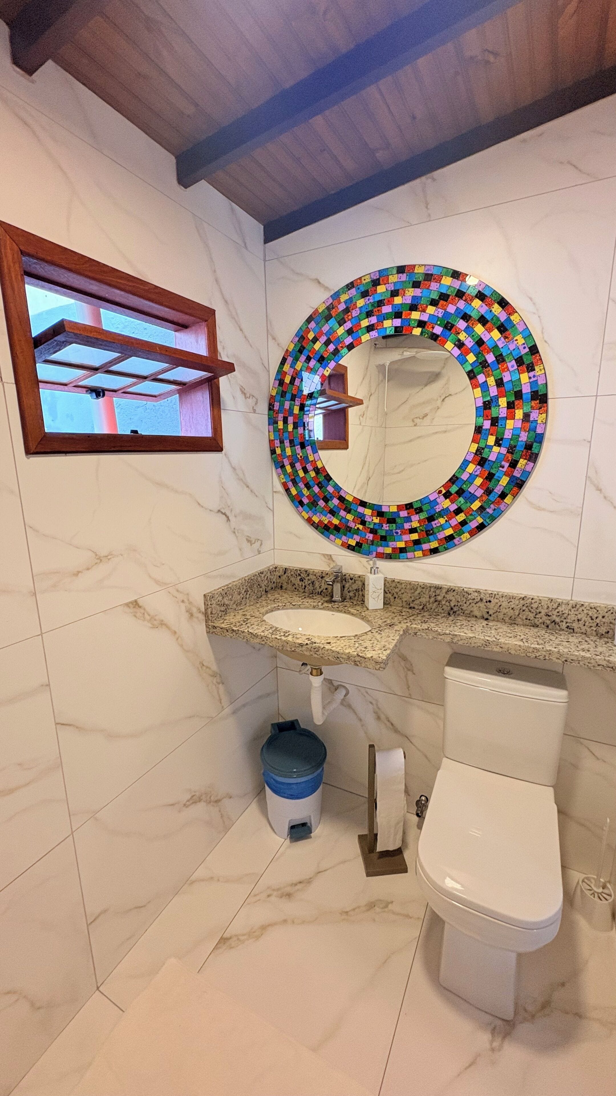 A bathroom with a marble floor, a sink with a granite countertop, a toilet, and a mirror with a colorful mosaic border.