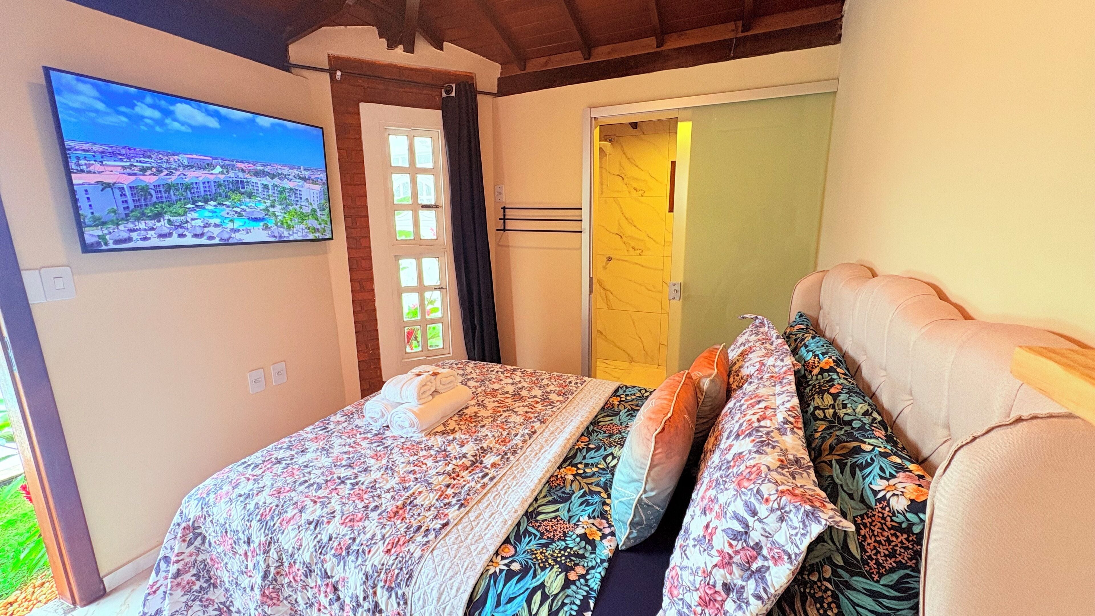 A bedroom with a bed, a television on the wall, and a door leading to another room.